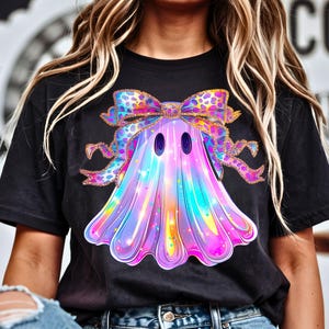 Op de afbeelding: Zwart t-shirt met een kleurrijk spookontwerp en een strik. Het spook is in tinten paars, blauw en roze, met een bijpassende strik. Het ontwerp is waarschijnlijk voor Halloween of een vergelijkbare feestdag.