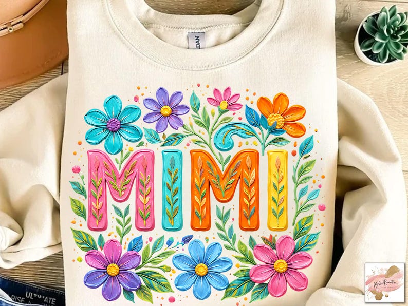 K&ouml;nnte beinhalten: Cremefarbenes Sweatshirt mit einem farbenfrohen Blumendesign und dem Wort "MIMI" in leuchtenden Buchstaben. Das Design zeigt rosa, orange, blaue und lila Blumen mit gr&uuml;nen Bl&auml;ttern, was eine fr&ouml;hliche und auff&auml;llige &Auml;sthetik erzeugt.