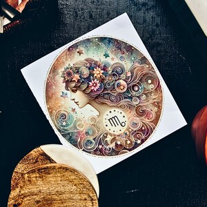 May include: A round, white paper print featuring a detailed illustration of a woman's profile with floral accents and a Virgo zodiac symbol. The artwork is surrounded by swirling patterns and stars, with a color palette of blues, pinks, and golds.
