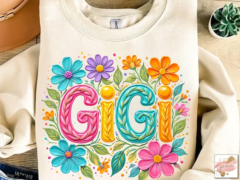 K&ouml;nnte beinhalten: Cremefarbenes Sweatshirt mit dem Wort "GIGI" in farbenfrohen, floralen Buchstaben. Das Design umfasst rosa, t&uuml;rkis, orange und lila Blumen mit gr&uuml;nen Bl&auml;ttern. Das Sweatshirt hat einen Rundhalsausschnitt und lange &Auml;rmel.