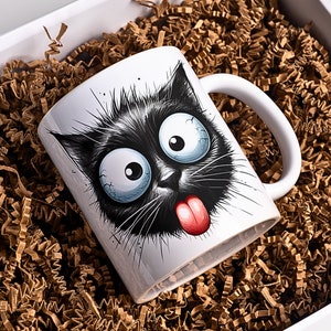 K&ouml;nnte beinhalten: Wei&szlig;e Keramiktasse mit einer Illustration einer schwarzen Katze. Die Katze hat gro&szlig;e, runde Augen, eine rosa Zunge, die herausstreckt, und einen schelmischen Ausdruck.