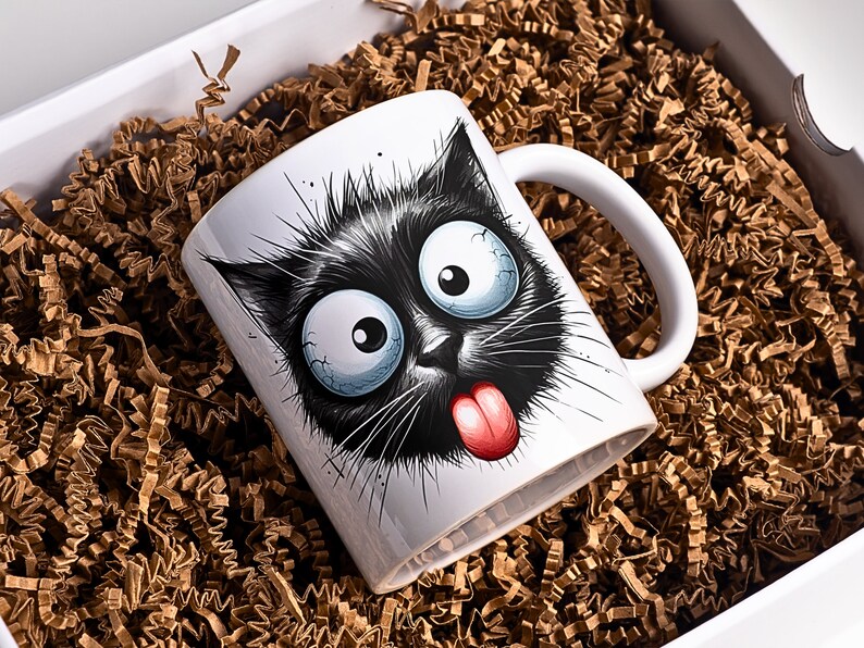 K&ouml;nnte beinhalten: Wei&szlig;e Keramiktasse mit einer Illustration einer schwarzen Katze. Die Katze hat gro&szlig;e, runde Augen, eine rosa Zunge, die herausstreckt, und einen schelmischen Ausdruck.
