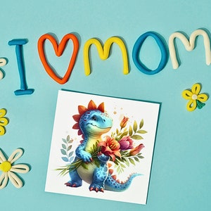 Puede incluir: Una tarjeta con un dinosaurio azul sosteniendo un ramo de flores. La tarjeta est&aacute; rodeada de letras de plastilina de colores que deletrean "I love mom".