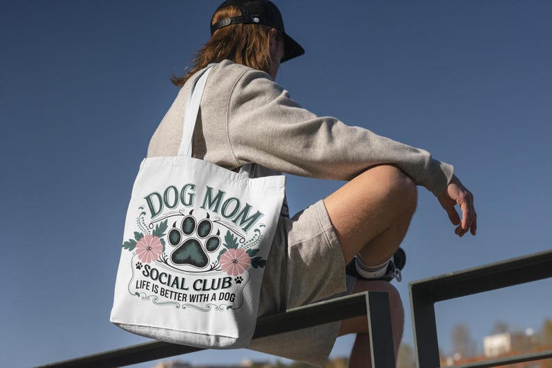 May include: White tote bag with a green and black paw print and floral design. The text on the bag reads "Dog Mom Social Club Life is better with a dog."