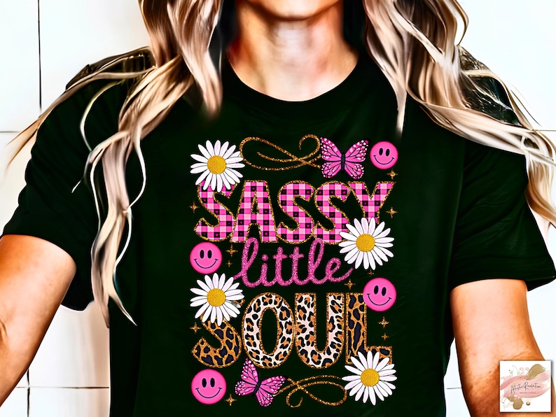 May include: Black t-shirt featuring a pink and black checked design that reads "Sassy little soul". The design also incorporates daisies, butterflies, and smiley faces.
