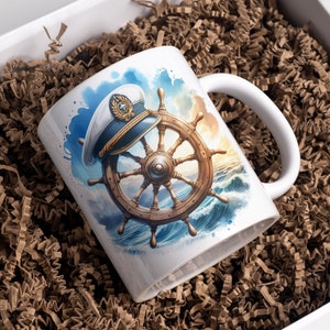 May include: White ceramic mug featuring a nautical design. The artwork depicts a ship's wheel and captain's hat against a backdrop of ocean waves and a sunset. The mug is presented in a white gift box with brown paper filler.