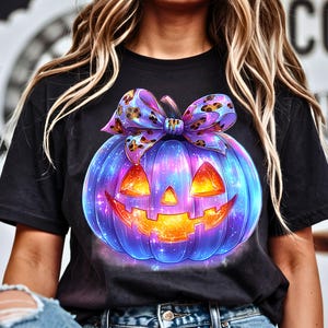 May include: Black t-shirt featuring a vibrant, glowing jack-o'-lantern design. The pumpkin is a mix of blue, purple, and orange with a patterned bow. The design is perfect for Halloween.