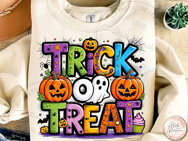 May include: A cream-colored sweatshirt featuring a colorful graphic with the text TRICK OR TREAT. The design includes two orange jack-o'-lanterns, a white ghost, a purple cupcake, spiderwebs, small spiders, and bats in vibrant shades.