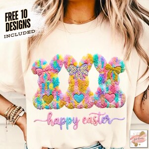 May include: A cream-colored t-shirt featuring three colorful bunny designs with bows and heart accents. The text "happy easter" is embroidered below the bunnies. The shirt also includes the text "FREE 10 DESIGNS INCLUDED".