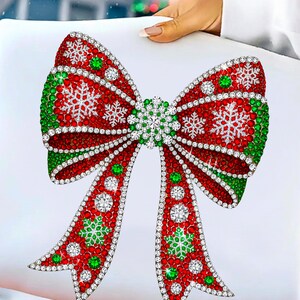 Puede incluir: Un dise&ntilde;o decorativo de lazo navide&ntilde;o, con una combinaci&oacute;n de colores rojo y verde y acentos de copo de nieve. El lazo est&aacute; adornado con brillantes pedrer&iacute;a, creando un aspecto festivo y elegante. El dise&ntilde;o est&aacute; sobre un fondo blanco.