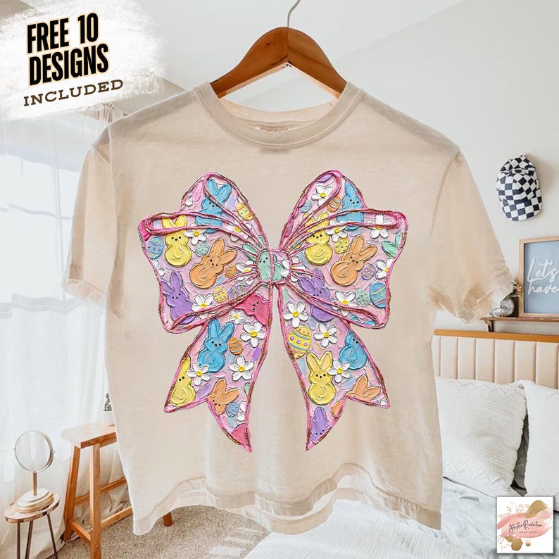 May include: A light beige t-shirt featuring a large, colorful bow design. The bow is decorated with Easter-themed elements, including bunnies, eggs, and flowers. The text "FREE 10 DESIGNS INCLUDED" is in the upper left corner.