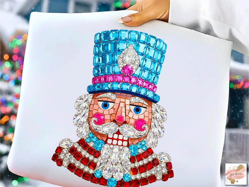 Puede incluir: Un coj&iacute;n decorativo con un dise&ntilde;o detallado de cascanueces enjoyado. El cascanueces tiene un sombrero azul, detalles en rosa y un uniforme rojo y blanco. El dise&ntilde;o est&aacute; hecho de cristales y gemas brillantes, creando un tema festivo navide&ntilde;o.
