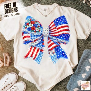 May include: White t-shirt featuring a large bow design with a patriotic theme. The bow incorporates elements of the American flag, with red and white stripes, blue stars, and floral accents. The text "FREE 10 DESIGNS INCLUDED" is visible.