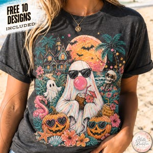 Op de afbeelding: Een donkergrijs t-shirt met een grafische print van een geest met een zonnebril die een roze kauwgombel blaast, omringd door een spookhuis, palmbomen, een grote oranje maan, vleermuizen, pompoenen met zonnebrillen en een skelet.