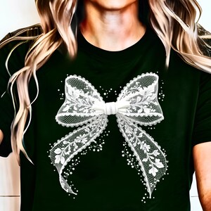 Puede incluir: Una camiseta negra con un dise&ntilde;o de lazo de encaje blanco. El lazo est&aacute; decorado con patrones florales y tiene un adorno de perlas.