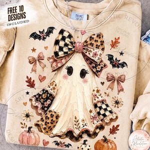 Puede incluir: Una sudadera beige con un gráfico central de un fantasma que lleva un lazo grande con patrones de cuadros y leopardo. El fantasma está rodeado de murciélagos, calabazas, flores y lazos pequeños en tonos naranja, negro y rosa. Texto: FREE 10 DESIGNS INCLUDED.