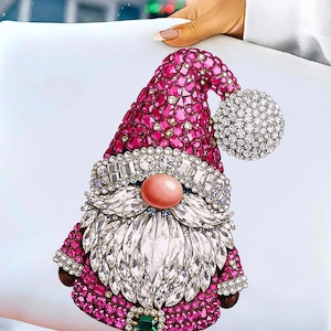 Puede incluir: Un dise&ntilde;o decorativo de gnomo navide&ntilde;o con sombrero y abrigo rosas, adornado con cristales brillantes. El gnomo presenta una barba de cristal blanca, una nariz rosa y una bola de cristal. Una decoraci&oacute;n festiva.