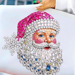 Puede incluir: Un coj&iacute;n decorativo con un dise&ntilde;o detallado de Pap&aacute; Noel. La imagen de Pap&aacute; Noel est&aacute; adornada con cristales brillantes en tonos rosa, blanco, azul y dorado. Un gran copo de nieve de cristal est&aacute; en el lado izquierdo.