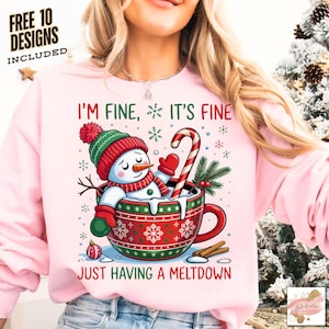 以下が含まれることがあります： 「I'M FINE, IT'S FINE JUST HAVING A MELTDOWN」の文字が入った赤いマグカップに入った雪だるまのグラフィックが特徴のピンク色のスウェットシャツ。雪だるまは赤と緑の帽子、スカーフ、ミトンを着用しています。キャンディケーンとシナモンスティックも表示されています。