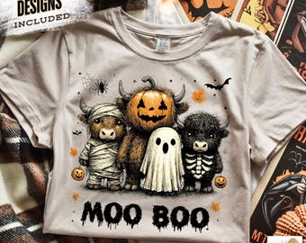 May include: Beige t-shirt with a Halloween-themed graphic. The design features three cartoon Highland cows dressed as a mummy, a jack-o'-lantern, and a skeleton, with the words "MOO BOO" below. The shirt includes the text "FREE 10 DESIGNS INCLUDED".