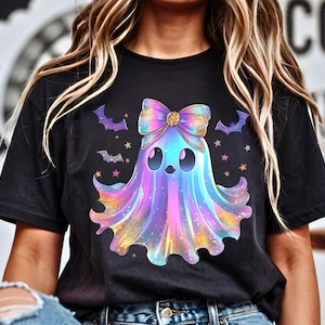 Puede incluir: Camiseta negra con un dise&ntilde;o de fantasma colorido, un gran lazo, murci&eacute;lagos y estrellas. El fantasma tiene una expresi&oacute;n linda y est&aacute; representado en tonos de azul, morado y amarillo. Un dise&ntilde;o divertido y caprichoso para Halloween.