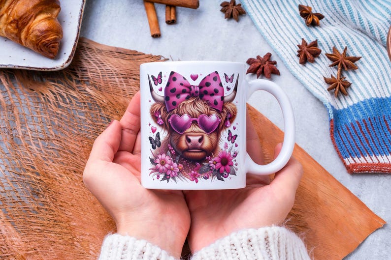 May include: White ceramic mug with a pink and black illustration of a Highland cow wearing pink sunglasses and a pink polka dot bow. The cow is surrounded by pink flowers.