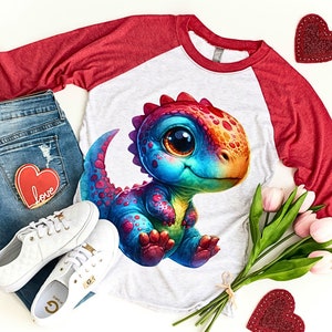 Puede incluir: Una camiseta de manga larga roja y gris con un gr&aacute;fico de dinosaurio arco&iacute;ris. El dinosaurio tiene ojos grandes y una expresi&oacute;n amigable. La camiseta es de estilo b&eacute;isbol con mangas rojas y cuerpo gris.