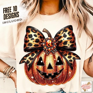 Può includere: T-shirt color crema con un design di zucca arancione glitterata, un volto sorridente nero e un fiocco leopardato. Il testo "FREE 10 DESIGNS INCLUDED" è stampato in nero. La zucca ha un centro gioiello.