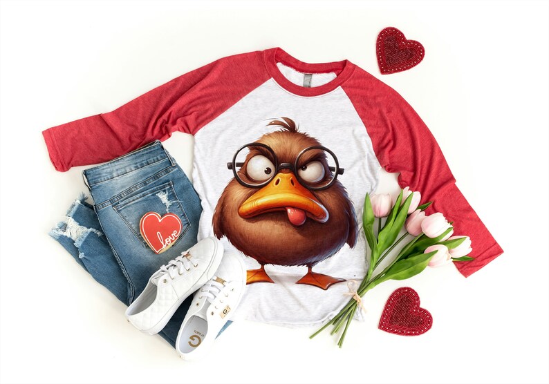 May include: A white and red baseball tee shirt with a brown cartoon duck wearing glasses and sticking out its tongue. The shirt is laying on a white surface with a pair of white sneakers, blue jeans, and a bouquet of pink tulips.