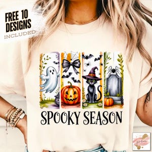 May include: Cream-colored t-shirt with a Halloween-themed design. The design includes a ghost, a bow, a jack-o'-lantern, a black cat in a witch hat, and a tombstone. The words "SPOOKY SEASON" are printed below the images. The text "FREE 10 DESIGNS INCLUDED" is printed at the top.