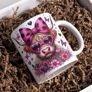 May include: White ceramic mug with a pink and black cow wearing pink heart-shaped sunglasses and a pink and black polka dot bow. The mug is surrounded by pink flowers and butterflies.