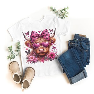 May include: White t-shirt with a pink and white cow wearing pink heart-shaped sunglasses and a pink polka dot bow. The cow is surrounded by pink flowers and butterflies.