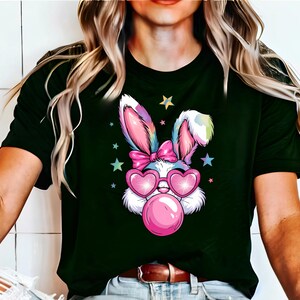 May include: A black t-shirt with a colorful cartoon bunny wearing pink heart-shaped sunglasses and blowing a pink bubble. The bunny has a pink bow on its head and is surrounded by stars.
