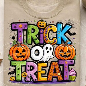 May include: A beige sweatshirt featuring a colorful graphic with the text TRICK OR TREAT. The design includes orange jack-o'-lanterns, a white ghost, a pink cupcake, spiders, spiderwebs, and bats, with each letter in a different bright color.