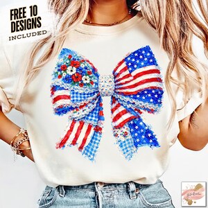 May include: Cream-colored t-shirt featuring a large bow design with an American flag theme. The bow incorporates red and white stripes, blue stars, and floral accents. The text "FREE 10 DESIGNS INCLUDED" is printed on the top left.