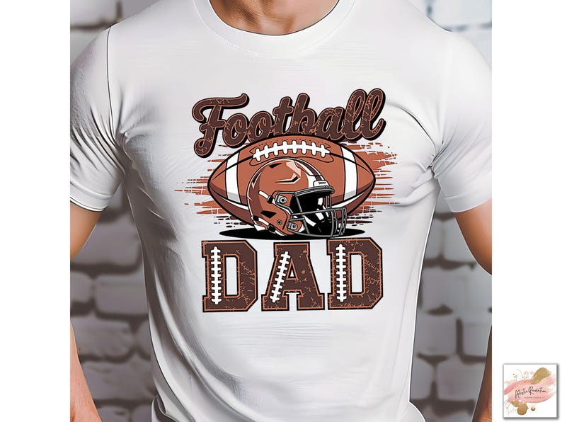 May include: White t-shirt featuring a football design. The design includes a brown football, helmet, and the words "Football DAD" in a brown, distressed font. The shirt is a classic crew neck.