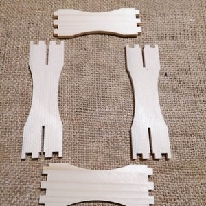 Puede incluir: Cuatro piezas de madera sin terminar para un proyecto de bricolaje. Las piezas tienen forma de rectángulos con recortes en los extremos. Las piezas están dispuestas sobre un fondo de arpillera.