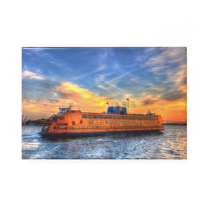 May include: An orange ferry boat with the text "CITY OF NEW YORK TRANSPORTATION" sails on the water. The sky is a mix of blue, orange, and yellow, creating a vibrant sunset scene.