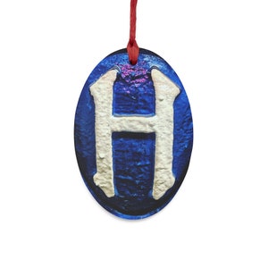 May include: A blue and white oval ornament with the letter "H" in white on a blue background. The ornament is hanging from a red string.