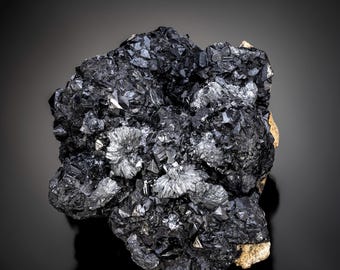 Może przedstawiać: Duży, ciemnoszary, metaliczny okaz mineralny o szorstkiej, fakturowanej powierzchni. Minerał ma krystaliczną strukturę z ostrymi krawędziami i wierzchołkami.