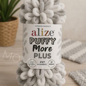 Op de afbeelding: Een bol Alize Puffy More Plus garen in wit en grijs. Het etiket luidt "100% Foon Polyester - Breien - Geen Naalden". Het garen is een gepatenteerd product.