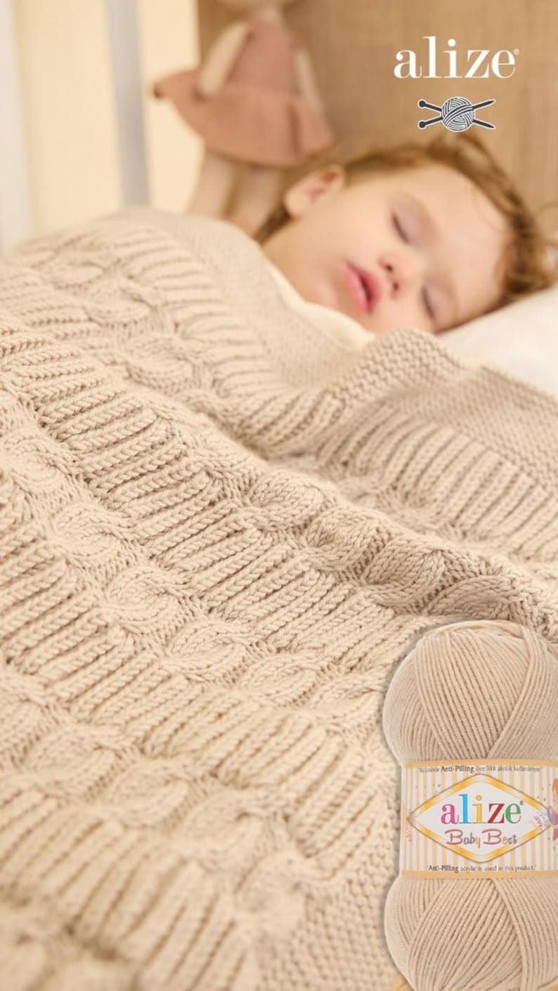 Puede incluir: Una manta de beb&eacute; de punto beige con un dise&ntilde;o de punto trenzado. La manta cubre a un ni&ntilde;o dormido. Se ve un ovillo de lana Alize Baby Best.