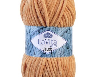 以下が含まれることがあります： ベージュ色のLaVita Velurの毛糸玉。ブランドロゴが入った水色のバンドで包まれています。柔らかく、ふわふわした毛糸で、編み物や手編みのプロジェクトに最適です。