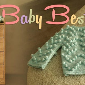 Puede incluir: Un c&aacute;rdigan de beb&eacute; verde menta con un dise&ntilde;o de punto de burbujas texturizado, junto con un gorro a juego. El c&aacute;rdigan tiene botones de madera. Tambi&eacute;n se ve un ovillo de lana Alize Baby Best. El texto "Baby Best" est&aacute; en la imagen.