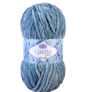 May include: A ball of blue-grey LaVita Velur yarn. The yarn is soft and plush, with a velvety texture. The label features the brand name and the word "VELUR" in a diamond shape.