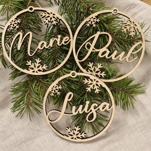 May include: Three wooden Christmas ornaments with the names Marie, Paul, and Luisa written in cursive. Each ornament has a snowflake design and a hole for hanging.