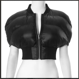 Puede incluir: Chaqueta corta acolchada negra con mangas cortas. La chaqueta presenta cuello y cintura de canalé, y cierre de cremallera plateada en la parte delantera. Las mangas abullonadas añaden un elemento de diseño único.