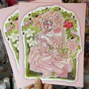 May include: A watercolor illustration of a pink fairy with blonde hair and green wings sitting in a garden. The fairy is wearing a pink dress with a green bow and is surrounded by flowers and strawberries.