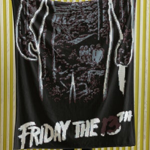 May include: Black and white pixelated blanket with the text "Friday the 13th" in white. A person is holding the blanket in front of a yellow striped wall.