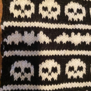 May include: Black and white knitted fabric with a pattern of skulls and bats. The fabric is made of a soft, fuzzy yarn.